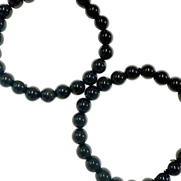 A black obsidian bracelet with round beads laid out on a white surface.