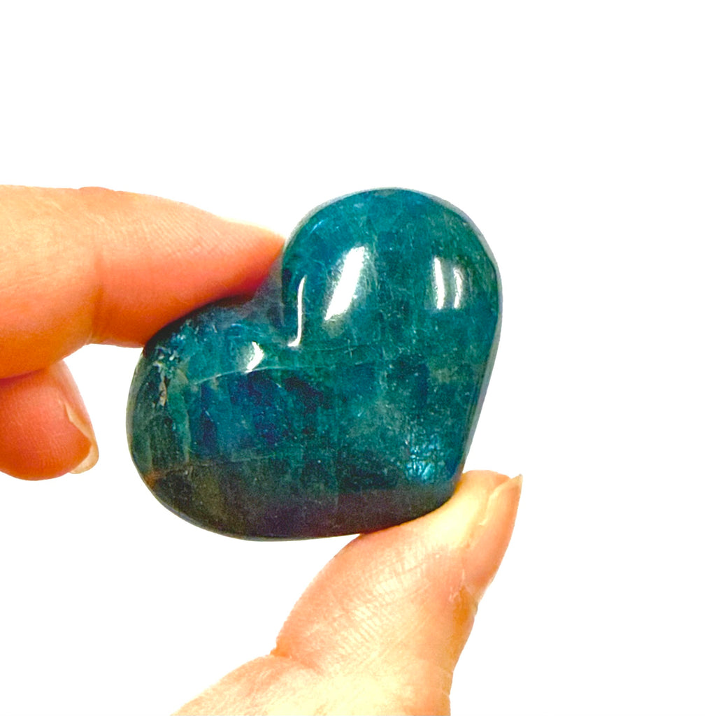 Heart-shaped blue apatite stone held between fingers against a white background