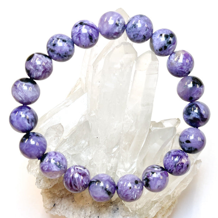 A bracelet made of polished Charoite beads with a variety of colors, displayed on a crystal.