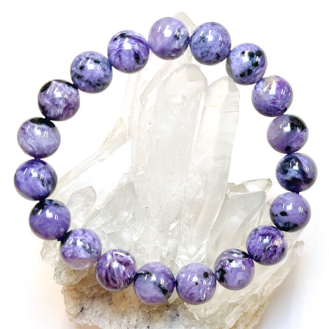 A bracelet made of polished Charoite beads with a variety of colors, displayed on a crystal.
