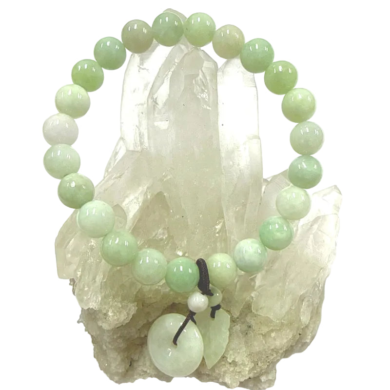 Green jade beaded bracelet with a leaf and donut charm on a crystal background