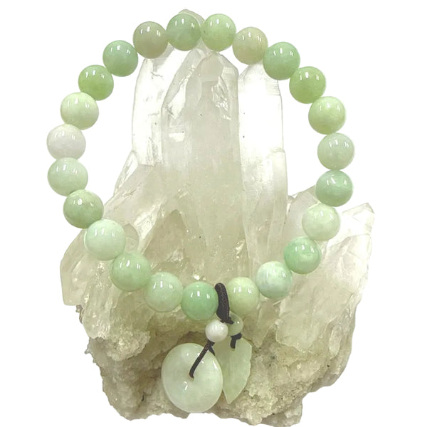 Green jade beaded bracelet with a leaf and donut charm on a crystal background