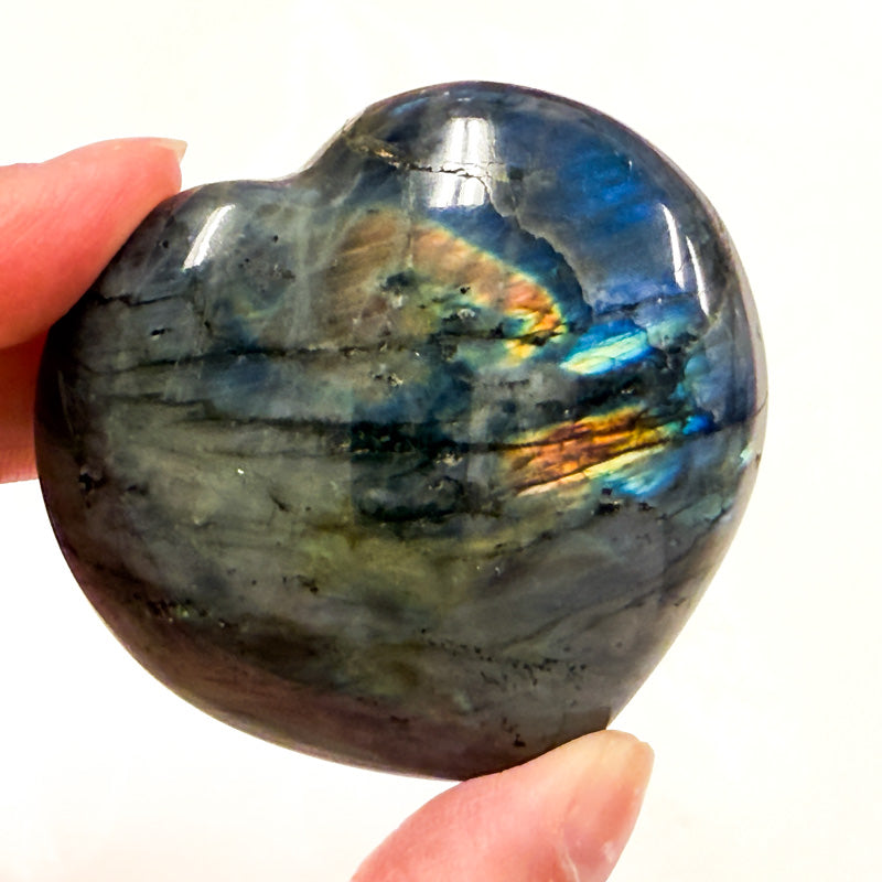 A heart-shaped labradorite crystal with a visible iridescent color spectrum, held in a person's hand.