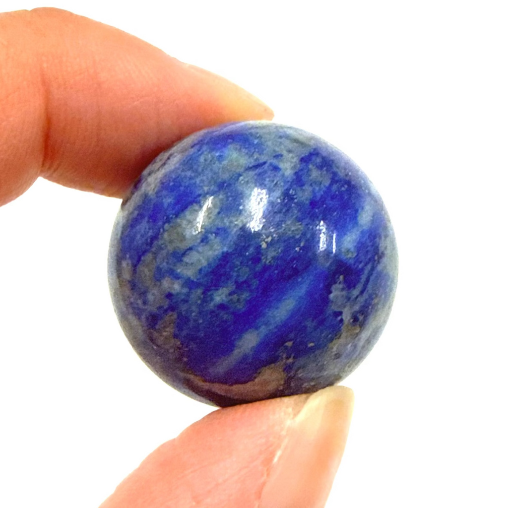 Lapis lazuli sphere 2.5cm stone held between fingers against a white background