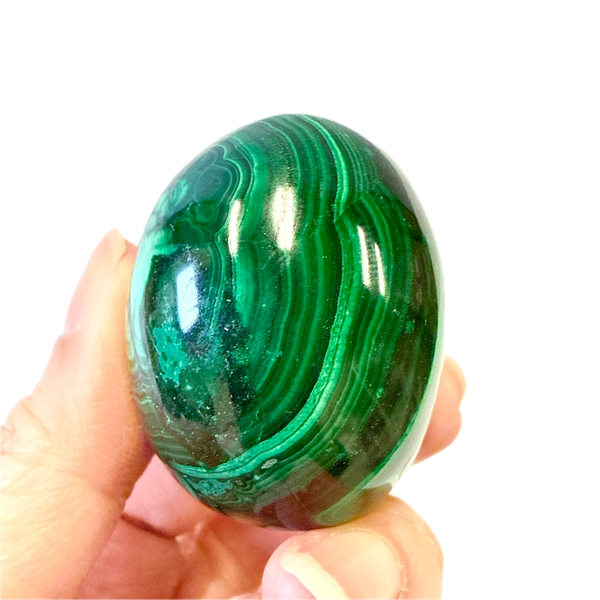 Hand holding a green malachite egg against a white background