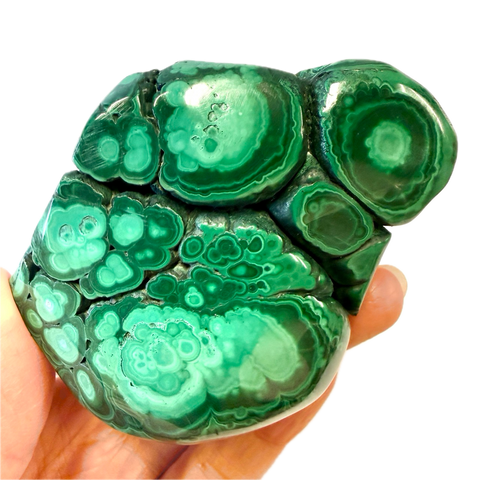 Green malachite stone held in a hand against a white background