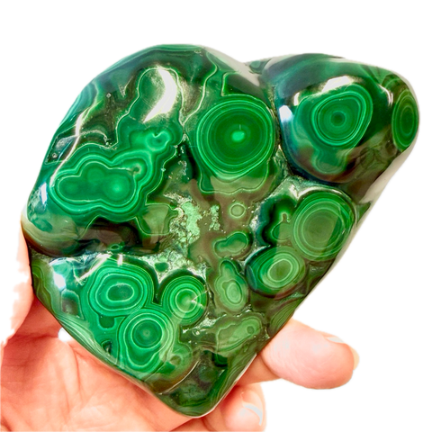 Hand holding a green malachite crystal with intricate patterns