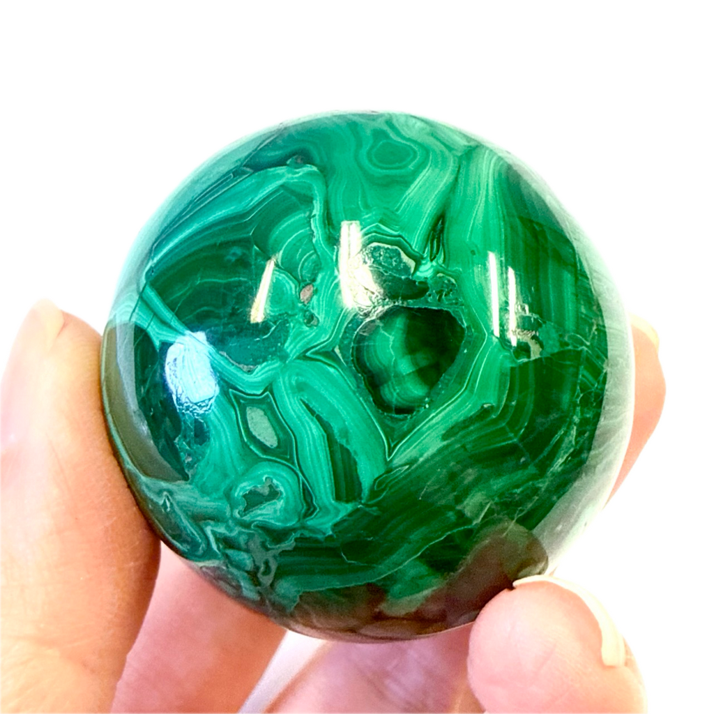 Green malachite crystal held in a hand against a white background