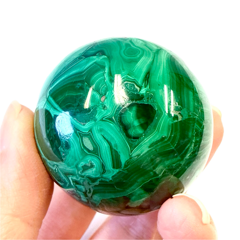 Green malachite crystal held in a hand against a white background