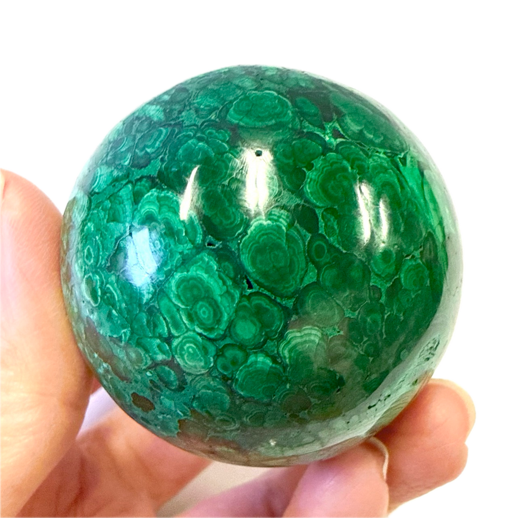 Green malachite sphere held in a hand against a white background
