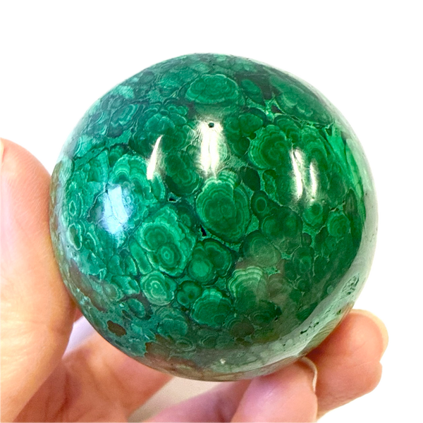 Green malachite sphere held in a hand against a white background