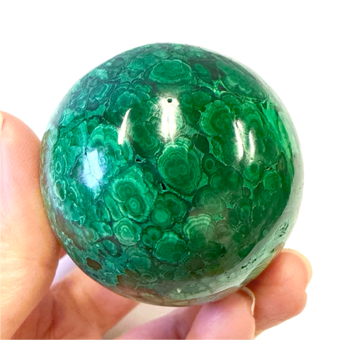 Green malachite sphere held in a hand against a white background