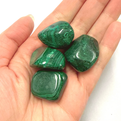 Hand holding three green malachite stones against a white background