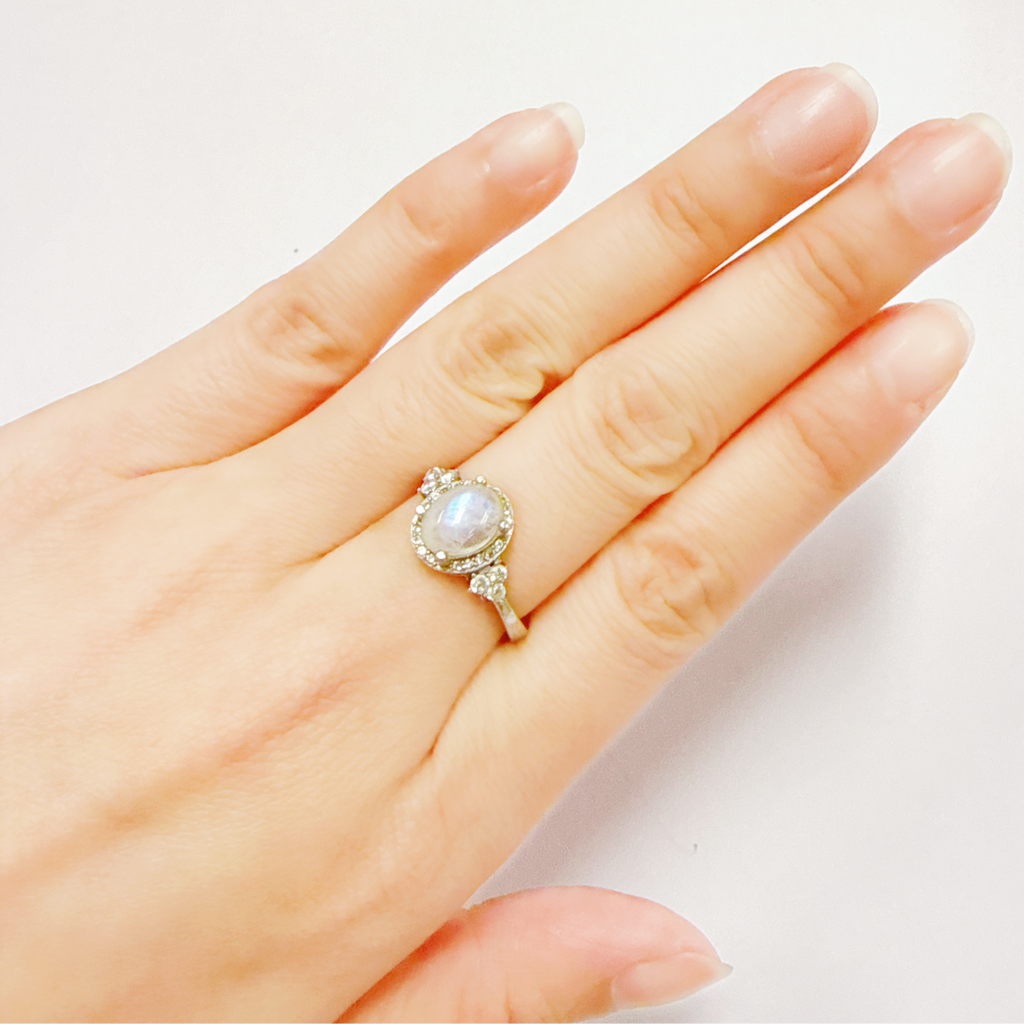 Hand wearing a ring with a moonstone gemstone on a light background