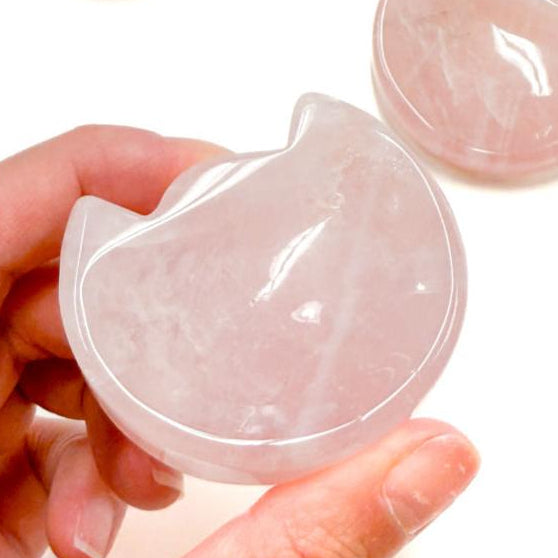 A hand holding a pink rose quartz crystal cat head shaped dish bowl, with another bowl partially visible in the background.