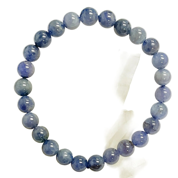 A tanzanite beaded bracelet with a variety of shades of blue, displayed on a crystal.