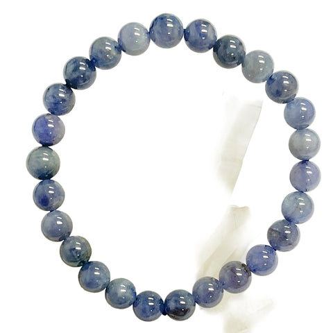 A tanzanite beaded bracelet with a variety of shades of blue, displayed on a crystal.
