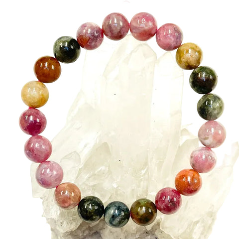 A multicolored tourmaline bracelet displayed on a crystal, with a mix of pink, green, brown, and red beads.