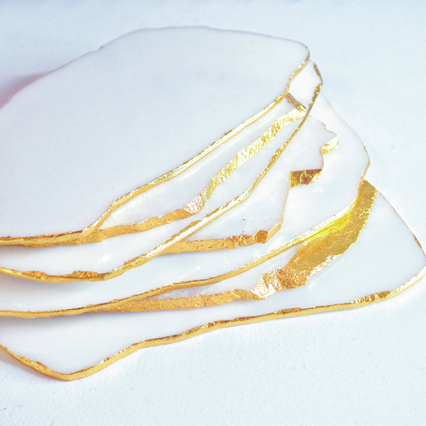 A stack of white quartz platters with gold accents on the edges, placed on a white surface.