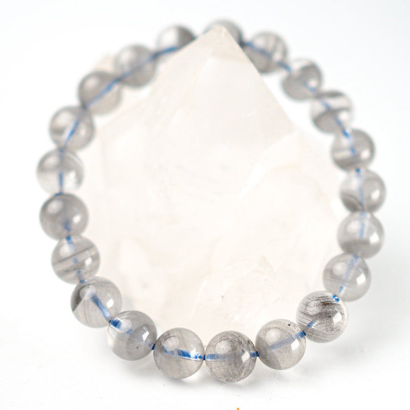 A bracelet made of grey tinted quartz beads with a striped pattern and a large clear quartz bead in the center, with an elastic stretching cord.