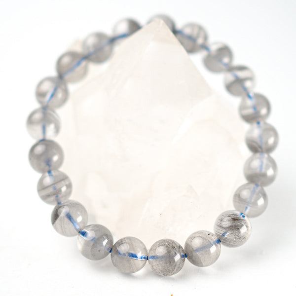 A bracelet made of grey tinted quartz beads with a striped pattern and a large clear quartz bead in the center, with an elastic stretching cord.