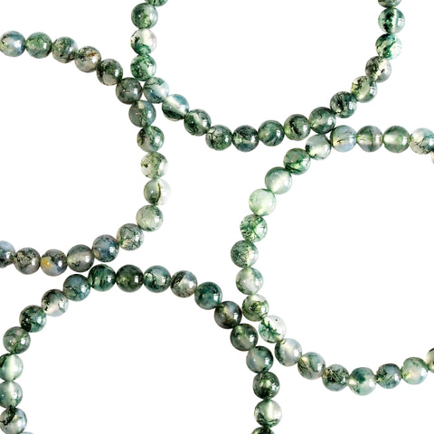A close-up image of a Moss Agate bracelet with green and clear patterned beads laid out on a white surface.