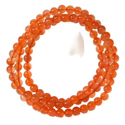 A red-colored bracelet or necklace made of rutilated quartz with reddish hair-like inclusions, displayed on a white background next to a transparent crystal.